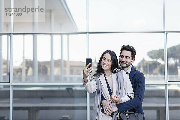 Professionelles Paar nimmt Selfie durch Handy vor dem Gebäude