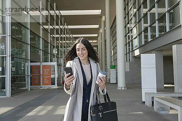 Junge Unternehmerin  die ein Mobiltelefon benutzt  während sie auf dem Gehweg steht