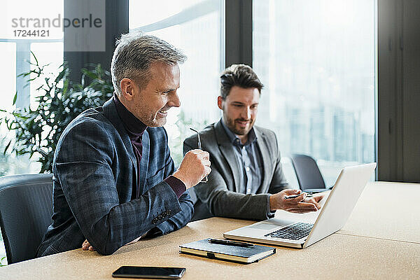 Lächelnde männliche Unternehmer  die über einen Laptop diskutieren  während sie im Büro arbeiten