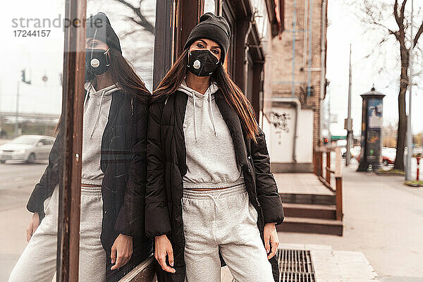Frau mit Strickmütze und Gesichtsschutzmaske lehnt sich an ein Glasfenster