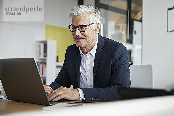 Lächelnder Unternehmer mit Laptop bei der Arbeit im Büro