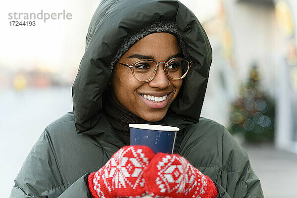 Lächelnde Frau mit wiederverwendbarem Becher und Handschuhen im Winter