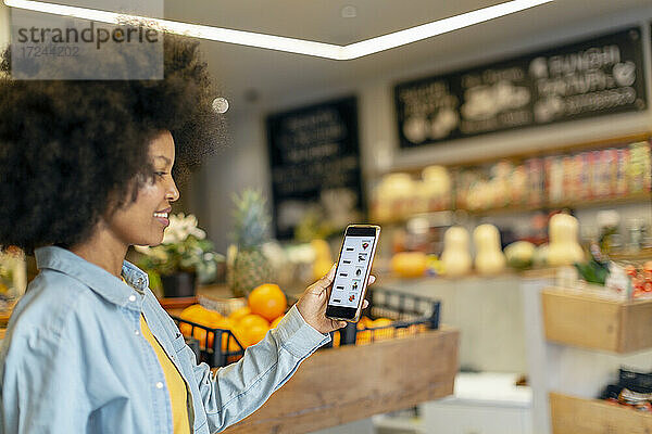 Afro-Frau  die eine mobile Anwendung in einem Lebensmittelgeschäft nutzt