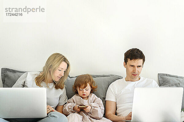 Geschäftsfrau mit Laptop  die ihre Tochter mit dem Mobiltelefon eines Geschäftsmannes beobachtet  der zu Hause arbeitet