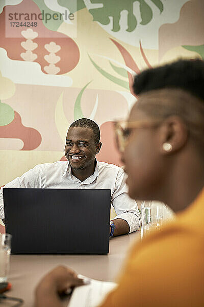 Geschäftsmann lächelnd mit Laptop am Schreibtisch sitzend während einer Besprechung im Büro