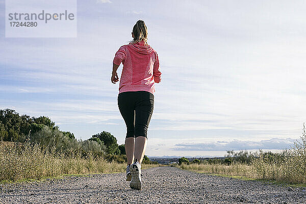 Weibliche Läuferin beim Joggen auf der Landstraße an einem sonnigen Tag