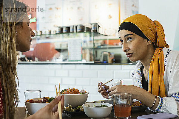 Junge Frauen unterhalten sich beim Essen im Restaurant miteinander
