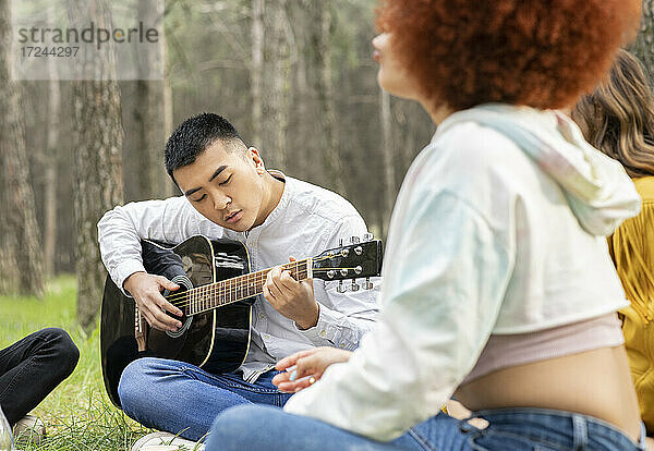 Mann spielt Gitarre  während er mit Freunden beim Picknick im Wald sitzt