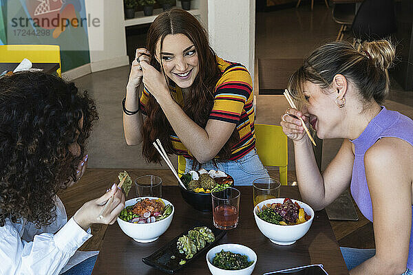 Glückliche multiethnische Freundinnen unterhalten sich beim Essen im Restaurant