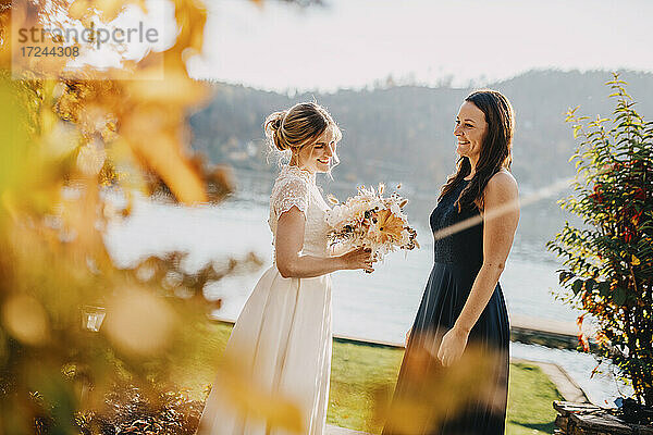 Glückliche Braut hält Blumenstrauß  während sie mit einem Freund steht