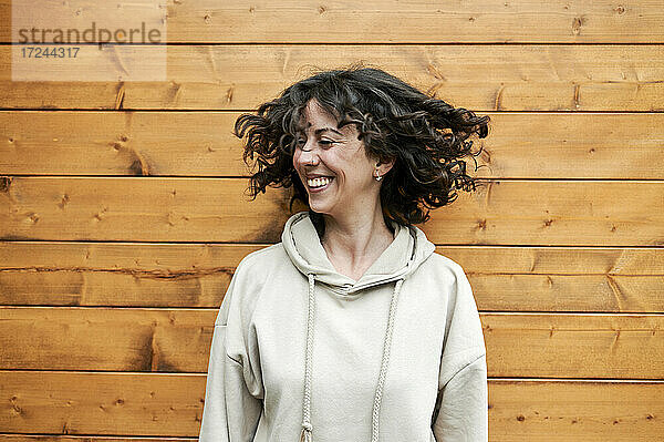 Lächelnde Frau  die sich die Haare zuwirft  während sie vor einer Holzwand steht