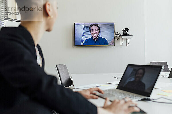 Geschäftsfrau  die an einer Besprechung mit einem Kollegen per Videoanruf über Laptop und Fernseher im Büro teilnimmt