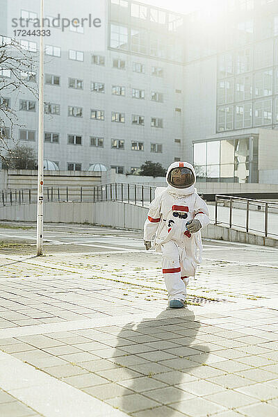 Junge Astronautin im Raumanzug  die an einem sonnigen Tag vor einem Gebäude spazieren geht