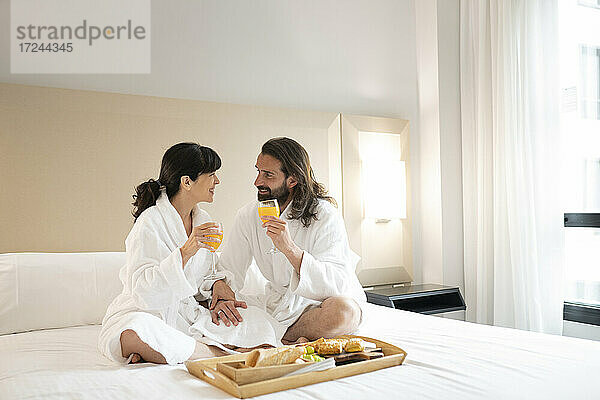 Paar in Bademänteln trinkt Saft auf dem Bett einer Hotelsuite