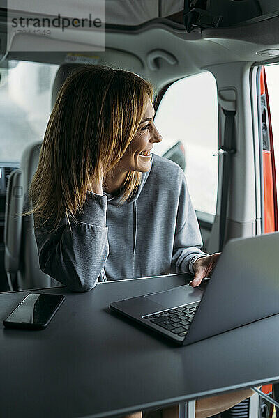 Weibliche Freiberuflerin schaut weg  während sie mit Laptop und Smartphone im Van sitzt