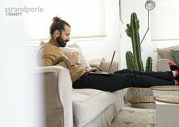 Entspannter Mann mit Tablet-PC auf dem Sofa im heimischen Wohnzimmer
