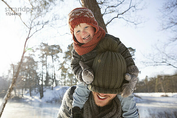 Lächelnder Sohn zieht seinem Vater im Winter die Strickmütze über das Gesicht