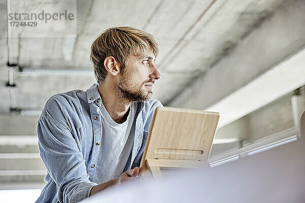Blonder Mann hält Holzmaterial und schaut weg  während er auf dem Dachboden steht