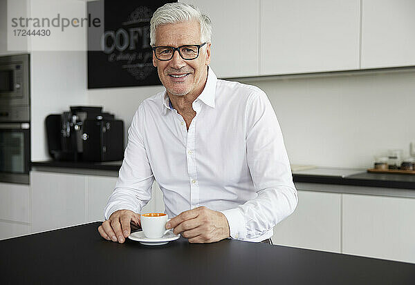 Lächelnder Geschäftsmann mit Brille sitzt mit einer Kaffeetasse in einer Cafeteria