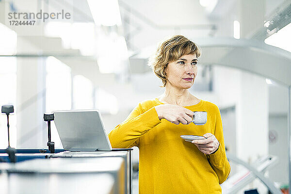 Nachdenkliche Geschäftsfrau mit Kaffeetasse in der Werkstatt stehend