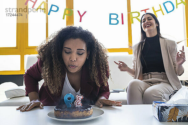 Weibliche Fachkraft bläst Geburtstagskerze auf Kuchen während einer Feier im Coworking-Büro aus
