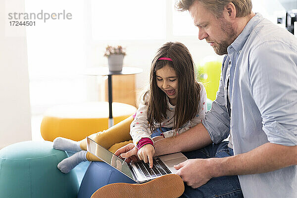 Verspieltes Mädchen sitzt bei ihrem Vater  der zu Hause am Laptop arbeitet