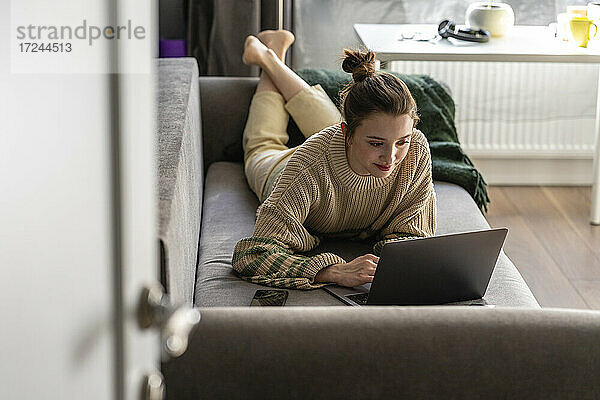 Junge Frau mit Laptop auf dem Sofa liegend