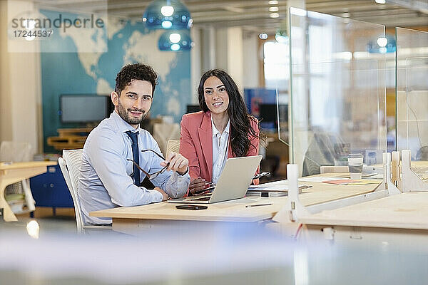 Männliche und weibliche Unternehmer sitzen lächelnd am Schreibtisch in einem Coworking-Büro