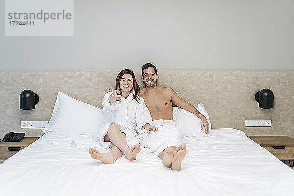 Entspanntes Paar  das auf dem Bett im Hotelzimmer sitzt und fernsieht