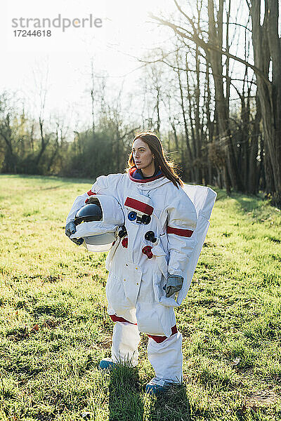 Weibliche Astronautin mit Weltraumhelm auf einer Wiese stehend
