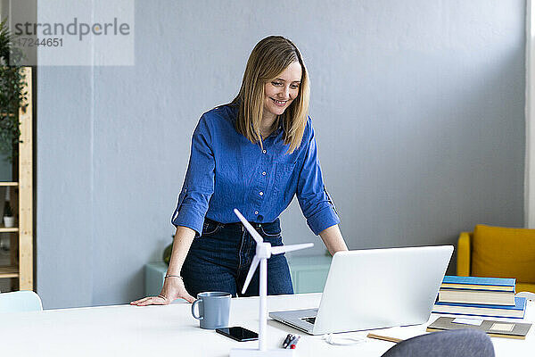 Geschäftsfrau lächelnd mit Blick auf Laptop im Büro