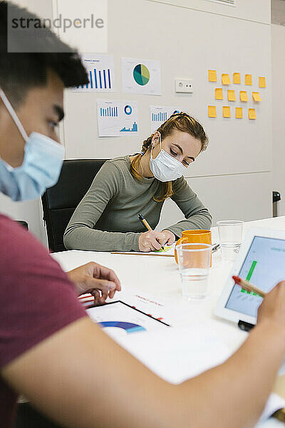 Geschäftsmann und Mitarbeiterin bei der Arbeit am Schreibtisch in einem Coworking-Büro während der COVID-19