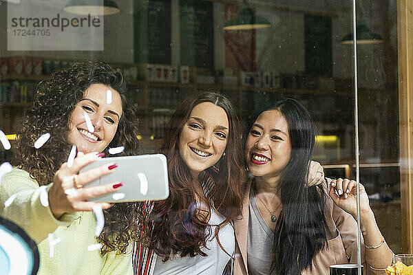 Freunde machen ein Selfie mit dem Handy am Fenster eines Cafés