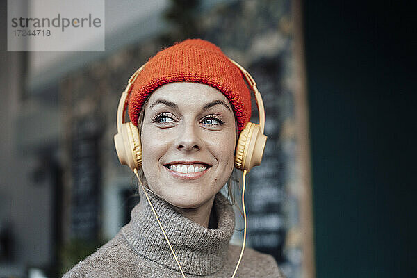 Lächelnde Frau hört Musik über Kopfhörer in einem Cafe