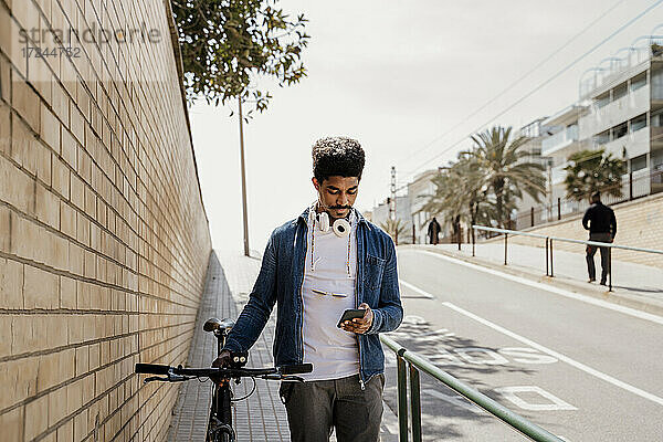 Gut aussehender Mann  der ein Mobiltelefon benutzt  während er mit dem Fahrrad auf dem Gehweg steht