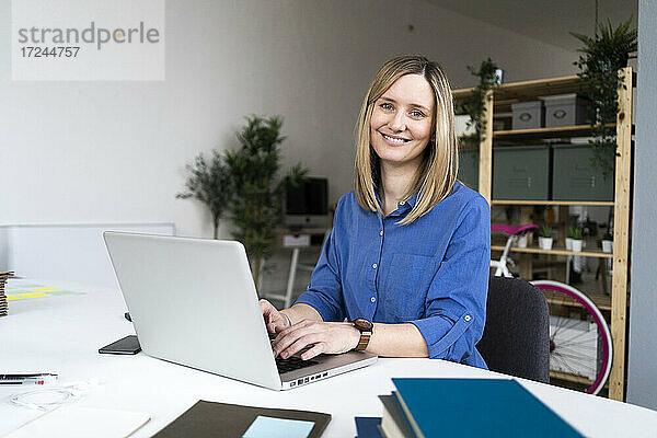 Lächelnde Geschäftsfrau beim Tippen auf einem Laptop im Büro