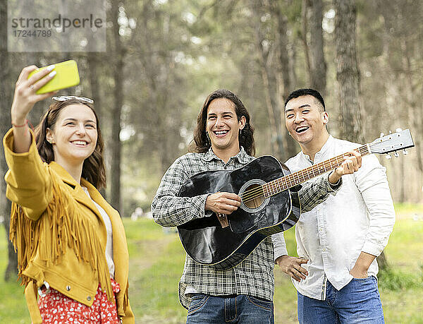 Schöne Frau nimmt Selfie mit männlichen Freunden auf Picknick im Wald