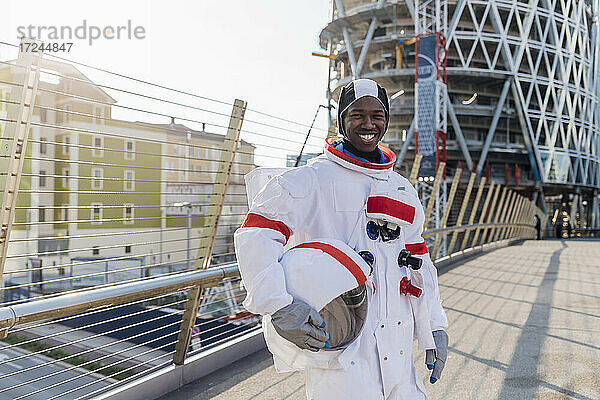 Lächelnder männlicher Astronaut mit Weltraumhelm auf einer Brücke in der Stadt stehend