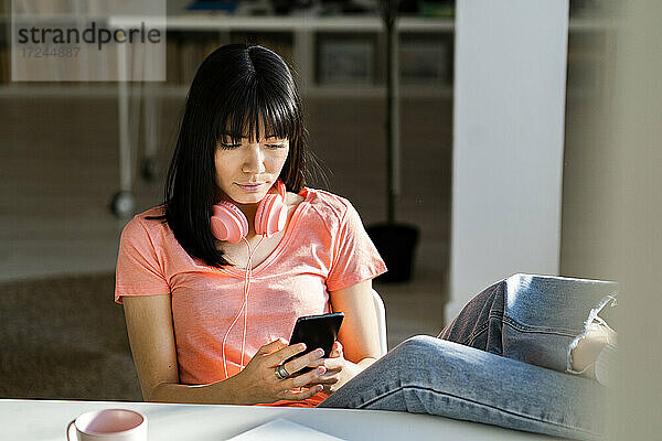 Junge Frau benutzt ein Smartphone  während sie zu Hause sitzt