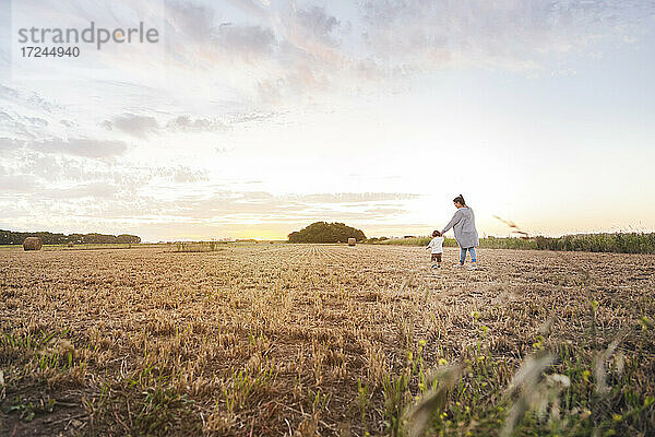 Mutter geht mit ihrem kleinen Sohn durch ein abgeerntetes Feld bei Sonnenuntergang