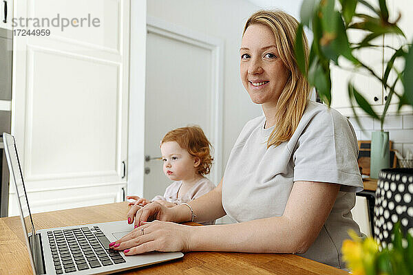 Lächelnde Geschäftsfrau mit Laptop bei ihrer Tochter in der Küche