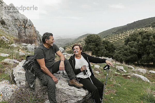 Älteres Paar beim Wandern in den Bergen  das lächelnd auf einem Felsen sitzt