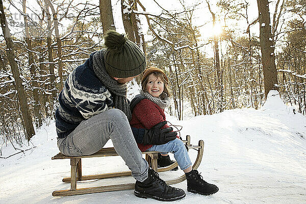 Vater sieht seinen Sohn an  während er im Winter auf dem Schlitten sitzt
