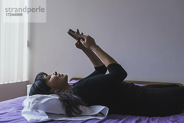 Mid Adult Frau Text-Messaging auf Smartphone im Schlafzimmer