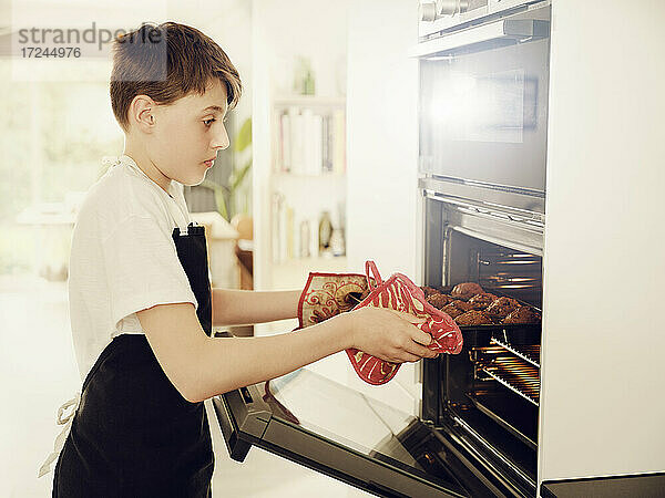 Junge nimmt Muffinblech aus dem Ofen in der Küche zu Hause