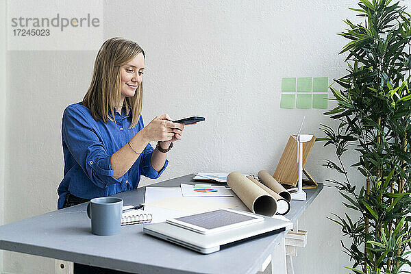 Geschäftsfrau mit Mobiltelefon am Schreibtisch im Büro sitzend