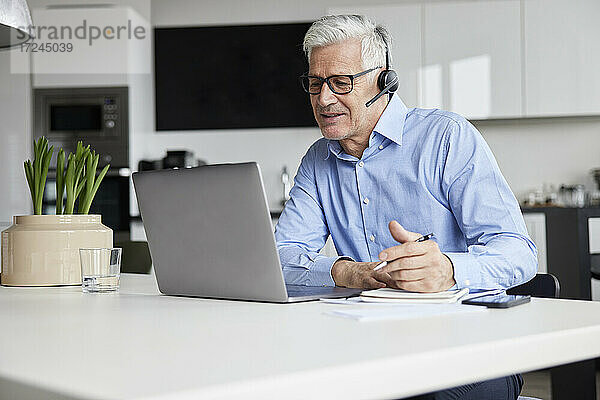 Älterer Berufstätiger mit drahtlosem Headset  der ein Videogespräch über einen Laptop im Büro führt