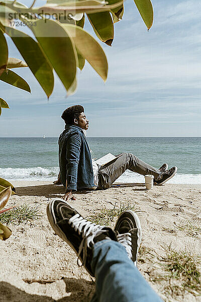 Entspannter Mann mit Buch am Strand sitzend an einem sonnigen Tag