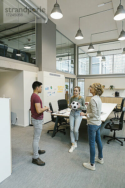 Männliche und weibliche Unternehmer spielen Fußball im Coworking-Büro