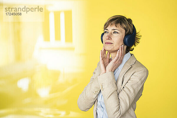 Nachdenkliche Geschäftsfrau mit Kopfhörern an einer gelben Wand